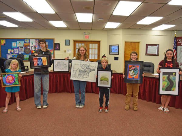 Gettysburg Area School District (GASD) students presented their art at the school board meeting Monday, May 19. Pictured from left are James Gettys Elementary first grader Emma Carter with her tempera painting, Gettysburg Area High School (GAHS) senior Madison Bensinger with her digital illustration, Gettysburg Area Middle School eighth grader Ruby Lancaster with her pen and ink piece, Franklin Township Elementary second grader Ellis Rice for his chalk pastels piece, Lincoln Elementary fifth grader Casey Cooke with a mixed media piece, and Franklin Township Elementary fifth grader Lillian Davis with a chalk pastels piece. Lancaster and Bensinger are also holding GAHS senior Sheng Hu's pencil drawing. (Photo Courtesy of GASD)
