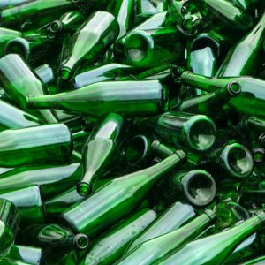 whole and broken green bottles, lie mountain on pavement. Concept: waste recycling, disposal of garbage and glass objects.