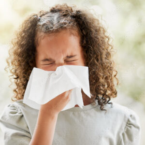 Sick little girl with a flu, blowing her nose and looking uncomfortable. Child suffering with sinus, allergies or covid symptoms and feeling unwell. Kid with a cold sneezing and holding a tissue