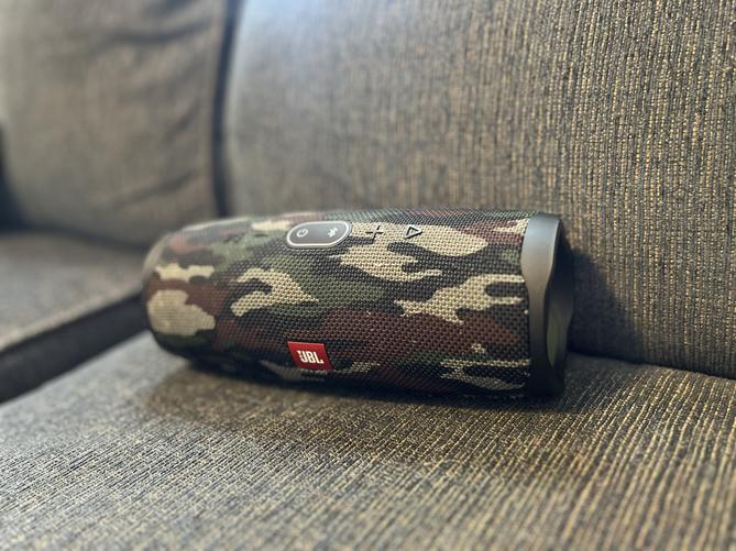 A Bluetooth speaker with a camouflage print sitting on a couch.
