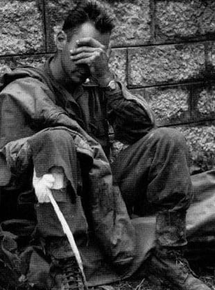 A weary World War II soldier sitting with his hand over his face